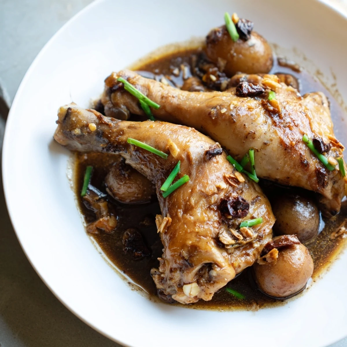 Filipino chicken adobo garnished with fresh green scallions featuring thick caramelized sauce coating crispy skin