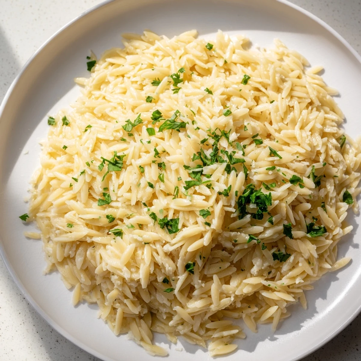 Golden orzo tossed with bright lemon zest, butter, and green parsley garnish on a rustic wooden table