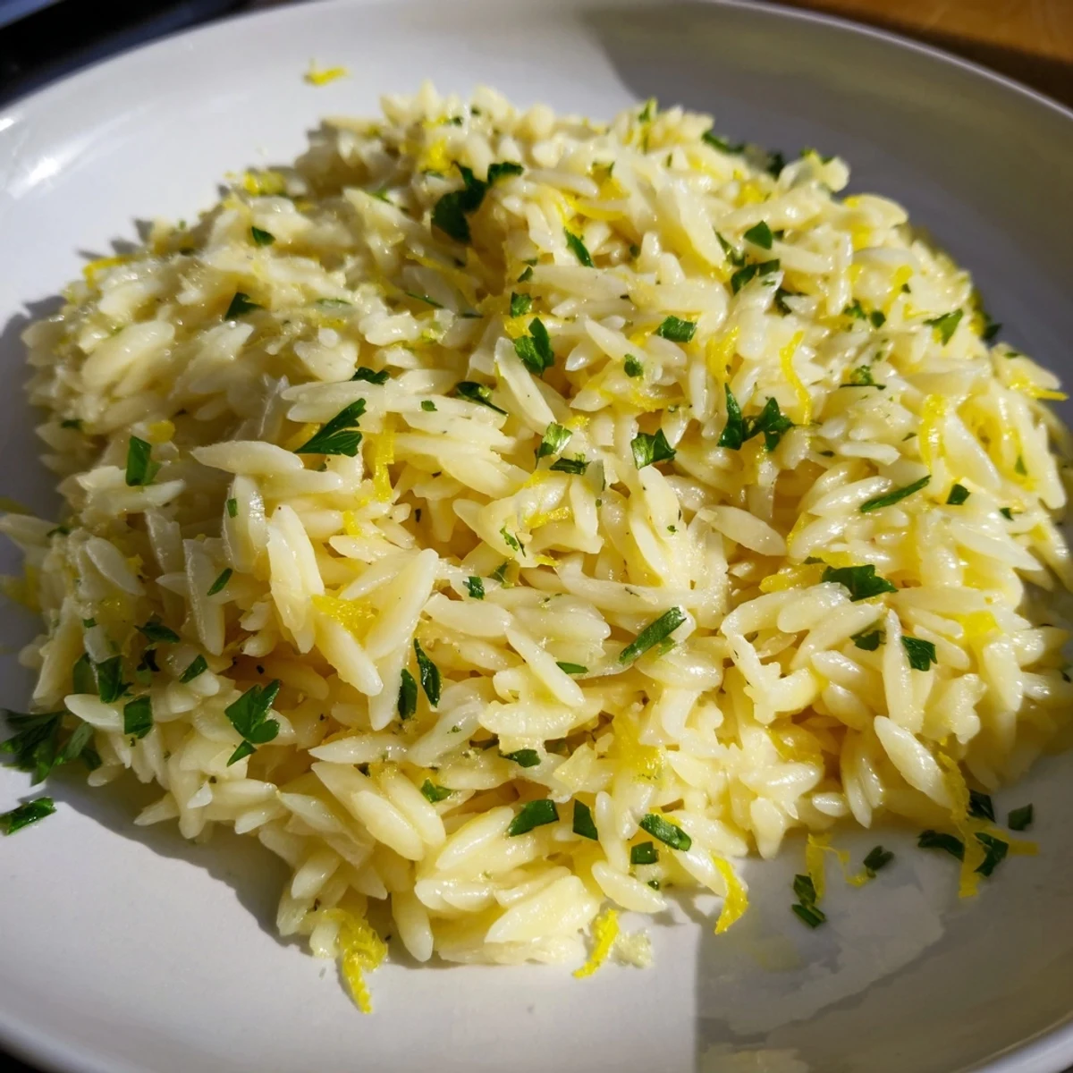 Creamy lemon orzo pasta topped with fresh parsley and grated Parmesan cheese in a white serving bowl