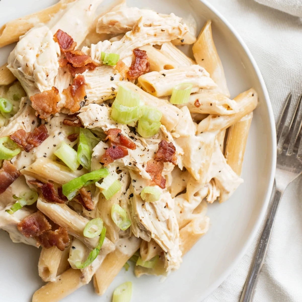 Comforting crack chicken pasta dish garnished with bacon bits and scallions on a rustic wooden table