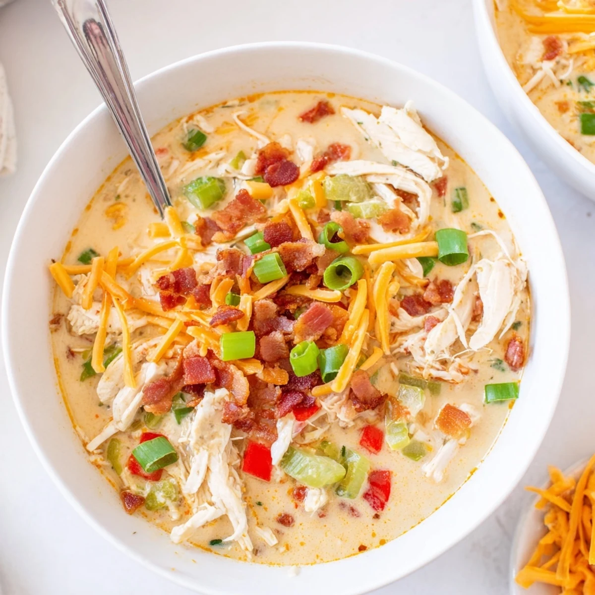 Creamy white spicy jalapeno popper chicken soup topped with crispy bacon crumbles and melted cheddar
