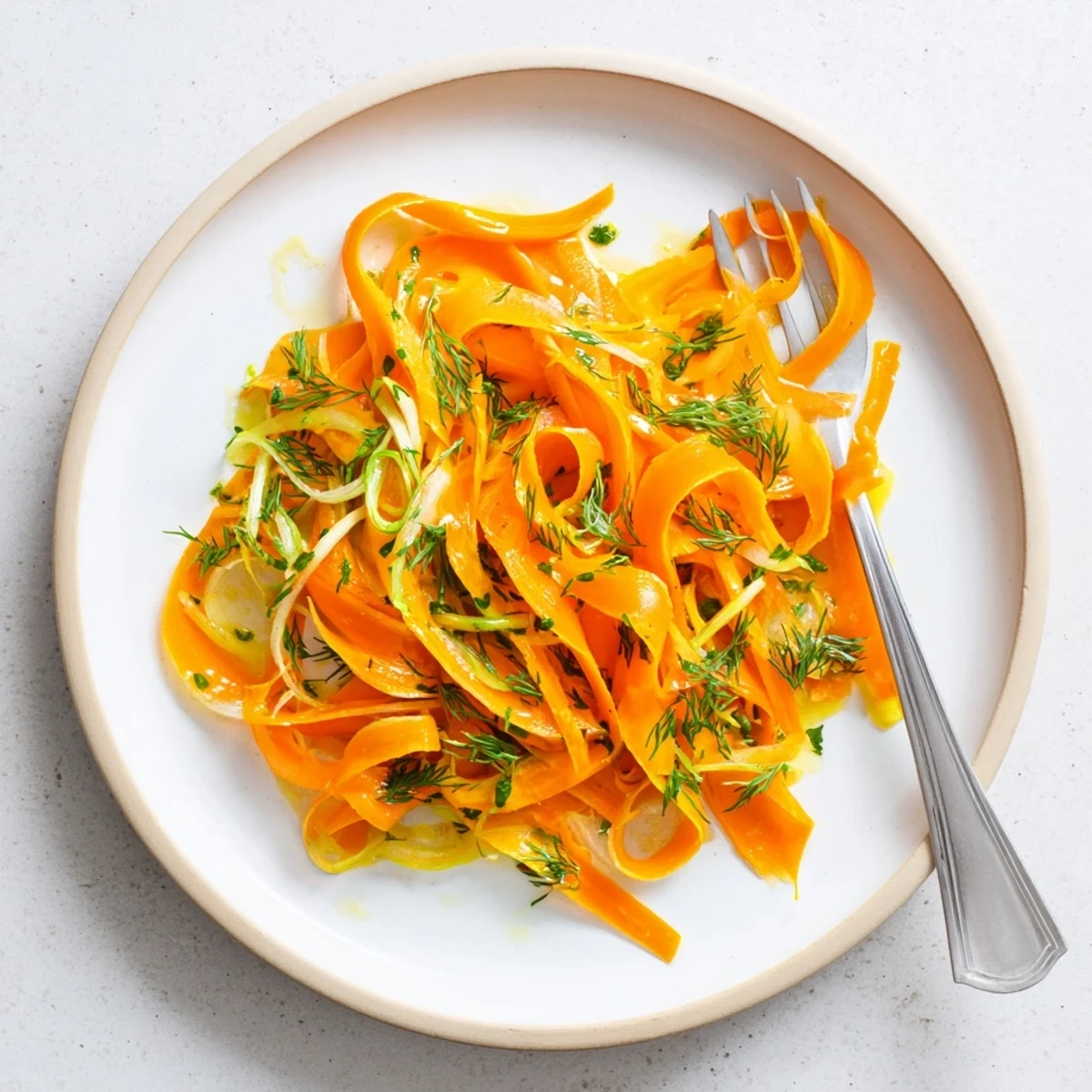 Tender julienned carrots tossed in zesty lemon and fresh dill marinade on white plate